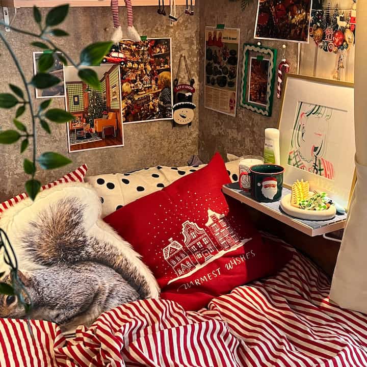 Cozy corner space with red and white striped bedding and Christmas-themed cushions, decorated with pictures and ornaments on the walls
