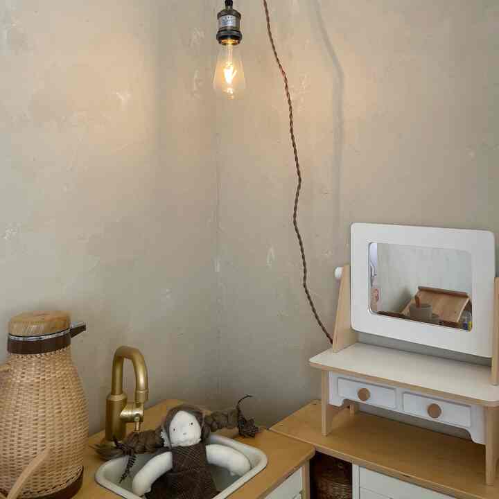 ナチュラルカラーの子供部屋、小さな木製家具とペンダントライトが配置された雰囲気のある空間