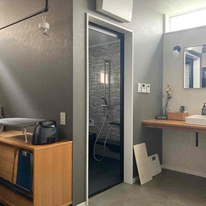 グレーとブラックのトーンのホテルライクなバスルーム、洗面台と木製家具が配置された清潔でゆったりとした空間