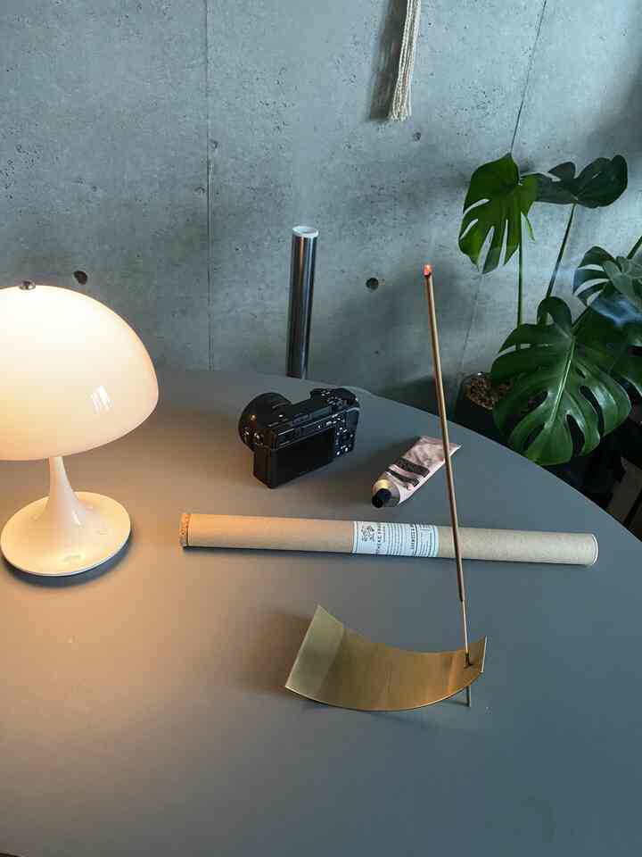 Gray-tone industrial style living room table featuring a lit incense stick with brass holder and white table lamp creating cozy ambiance