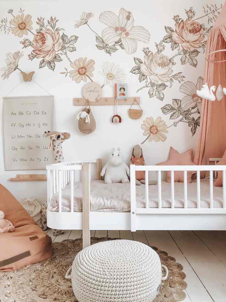 Beige and white toned kids' room featuring a white toddler bed, toys, and floral wall decor creating a warm atmosphere