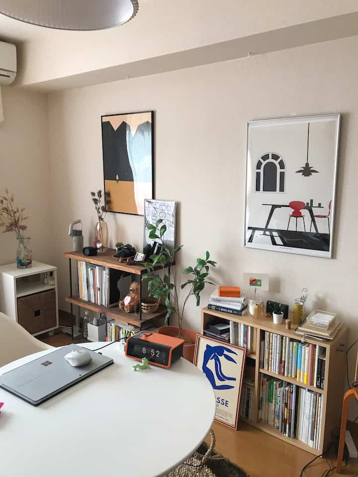 白い壁と木目調の家具が調和したホームオフィス、書棚とポスターが配置された雰囲気のある空間