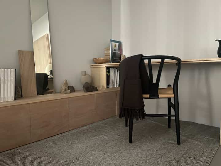 Natural modern workspace with a charcoal shawl draped over a Y Chair, featuring simple wood-toned cabinetry and desk setup