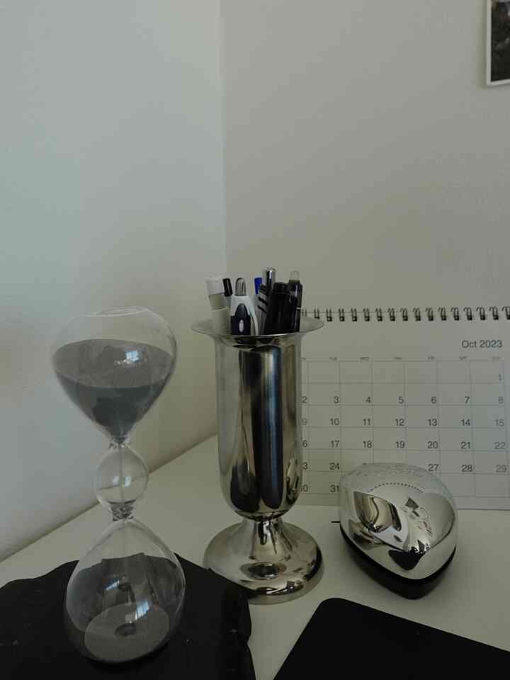 Clean home office space with white walls and desk featuring silver pen holder and hourglass