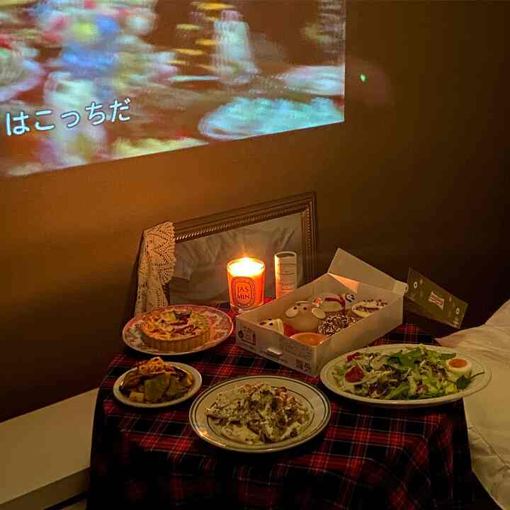 暖かい赤のテーブルランナーに料理とキャンドルが置かれた居心地の良いダイニング、壁に映るプロジェクター画面があるホームシネマ空間