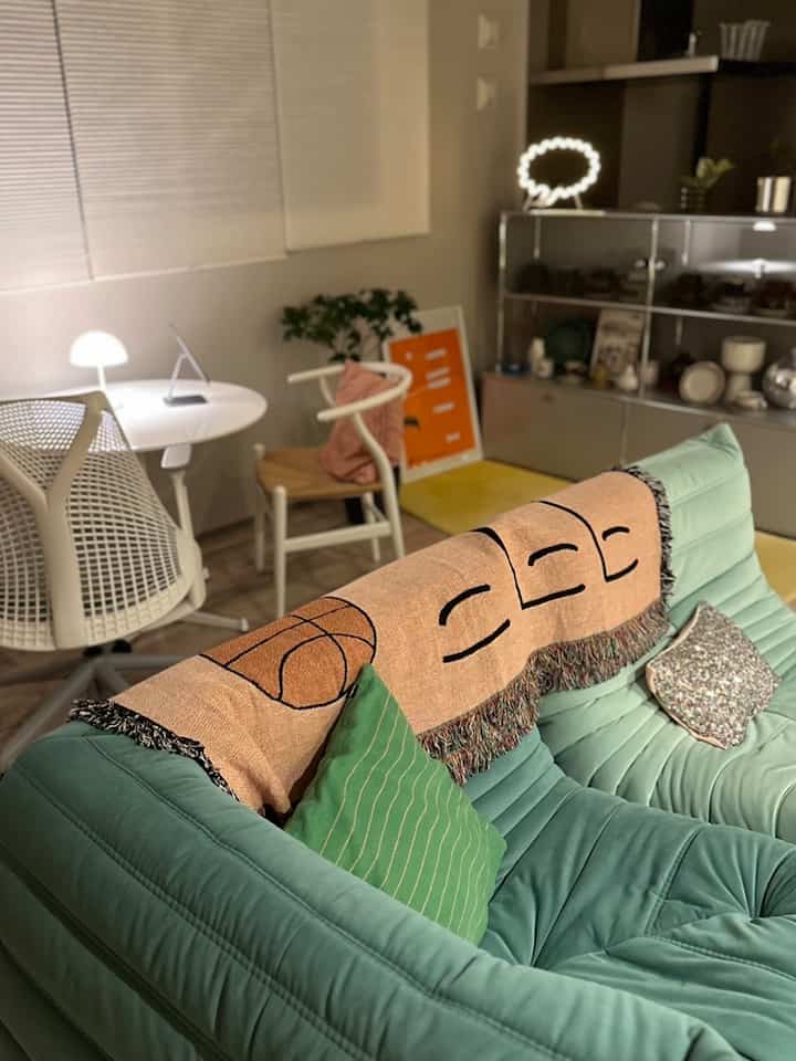 淡いグリーンとベージュ調のリビング、快適なソファにスローとクッションが配置された雰囲気のあるナチュラルモダンなインテリア