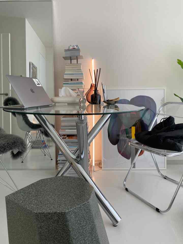 Minimal dining room in white and gray tones featuring a glass table and transparent chairs placed centrally with a bookshelf in the background