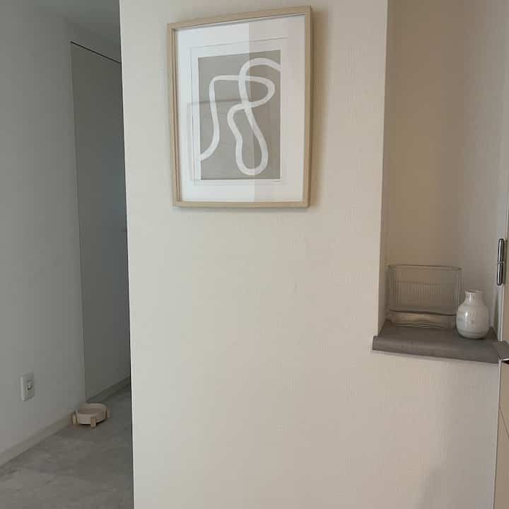 白とグレーの色調の玄関、シンプルなポスターと小物が置かれた清潔感のある雰囲気のインテリア