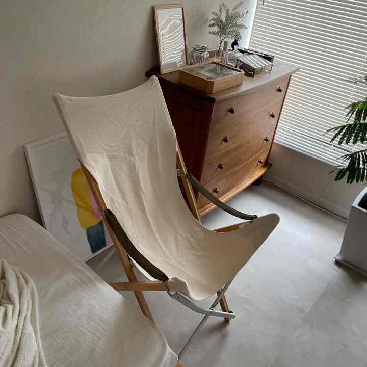 ベージュと木目調の寝室、キャンバス素材の折りたたみ椅子と木製チェストが落ち着いたナチュラルな雰囲気を演出するインテリア