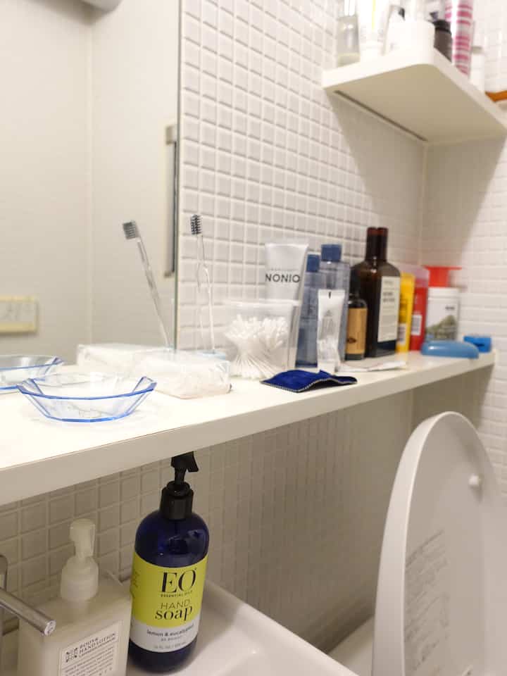 白いタイル壁と洗面台、棚にさまざまなバス用品が整頓された清潔感のあるバスルーム