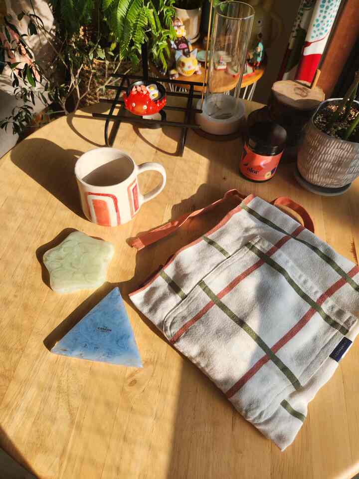 Natural wood-tone kitchen table featuring red and green accent coasters, apron, and mug in a cozy setting