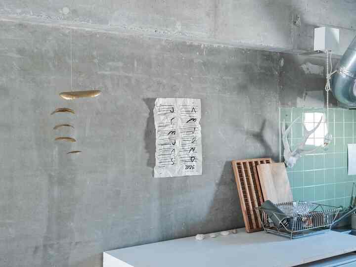 グレーのコンクリート壁とミントグリーンのタイルが調和したキッチンスペース、実用的なキッチン用品が配置された自然でインダストリアルな雰囲気のあるインテリア