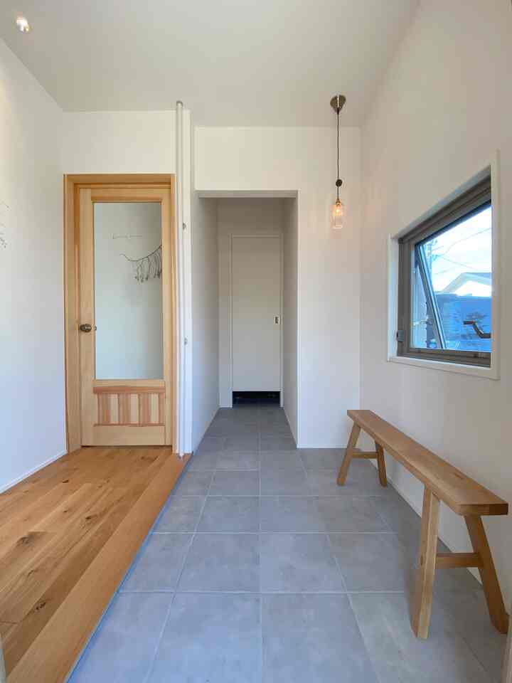 白い壁と木目調の家具が配置されたシンプルな玄関、ベンチとペンダントライトが調和する印象的な空間