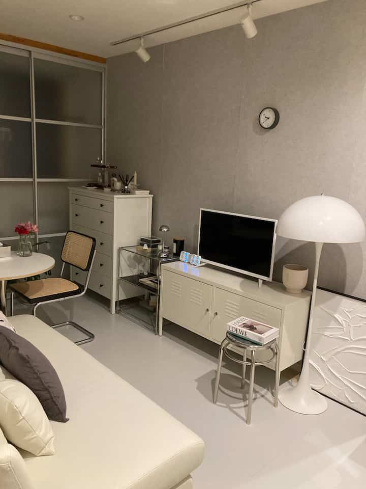 落ち着いたグレーの壁とホワイトの床、ソファとテレビスタンドが配置されたモダンなリビングルーム