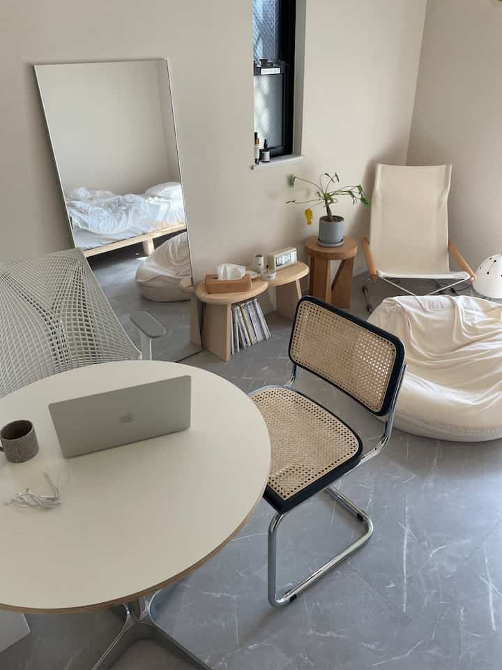 白とナチュラルカラーのリビング、丸テーブルとラタンチェア、ビーンバッグソファが配置されたシンプルなインテリア