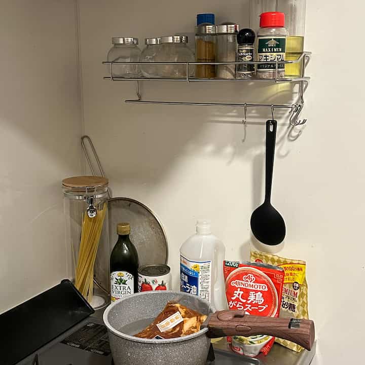 白い壁の小さなキッチン、グレーの鍋と整頓された調理器具、きちんと並べられた調味料が配置された雰囲気のあるインテリア