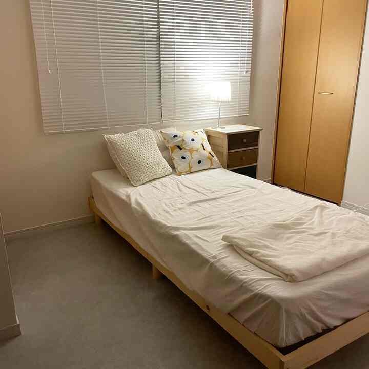 A white and wood-tone bedroom featuring a simple bed, nightstand with table lamp, creating a modern and calm atmosphere