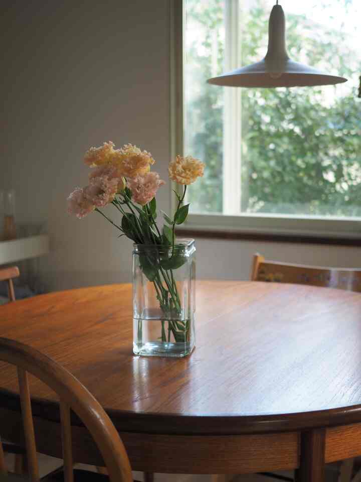 温かみのあるウッドトーンのヴィンテージダイニング、丸いチークのテーブルに透明な花瓶が置かれ、柔らかな花が彩る印象的な空間