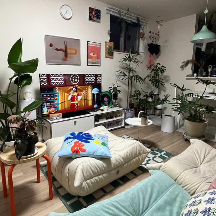 白い壁とキャラメルブラウンの床が特徴的な、2人暮らし向けのモダンなリビング、クリーム色のソファと多彩な植物が配置された空間