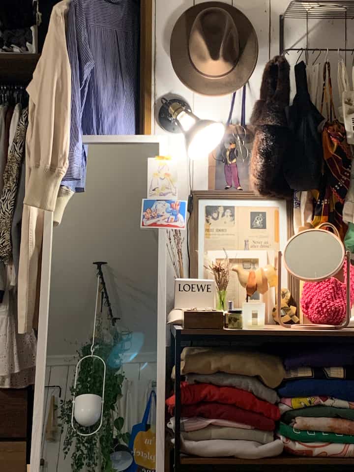A cozy walk-in closet space featuring a white wall and mirror, brown frames and hats, with organized clothing storage