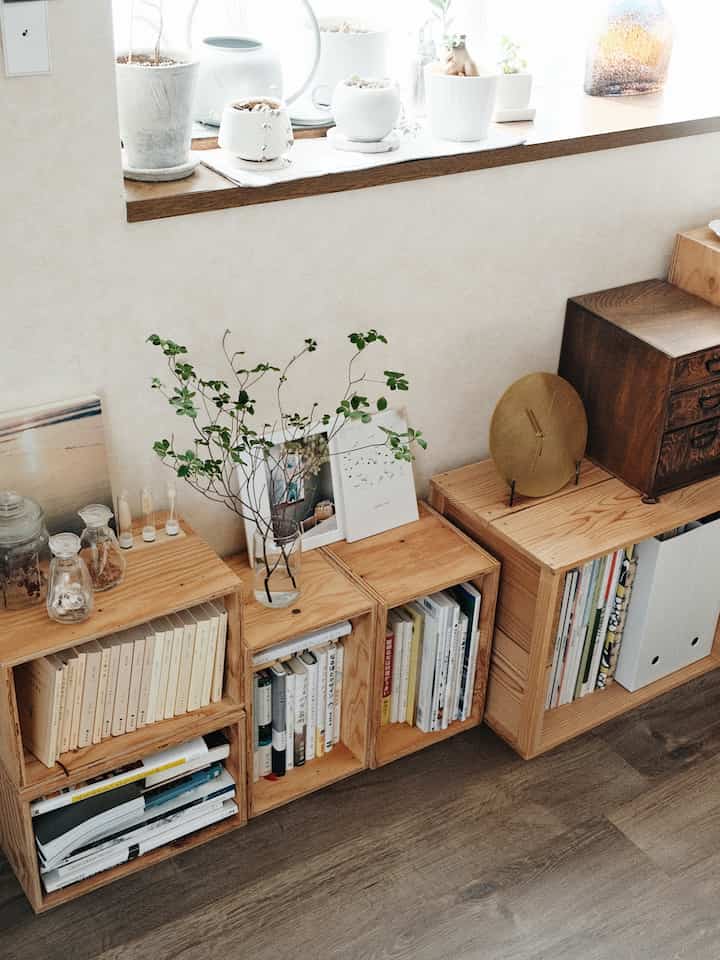 白い壁と木目調の本棚が配置されたシンプルで雰囲気のあるナチュラルな書斎、窓辺に複数の鉢植えが並ぶ