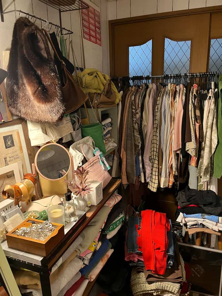 A cozy small walk-in closet in white and brown tones, featuring racks of clothes and shelves with folded items and accessories
