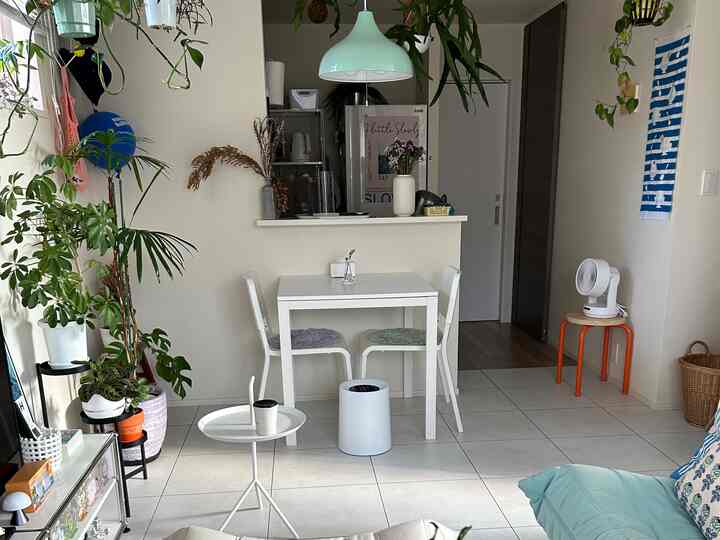 Small living room in white and natural tones featuring a compact dining table, chairs, and lush green plants creating a cozy atmosphere