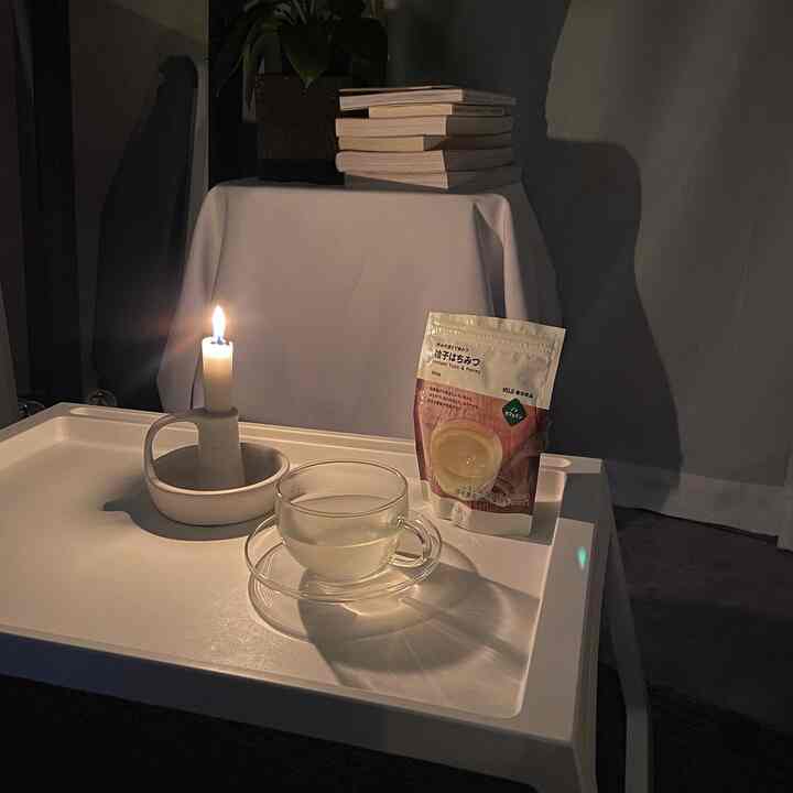 白を基調とした寝室、積み重ねた本とキャンドルの灯り、温かい飲み物が置かれた落ち着いた雰囲気のインテリア