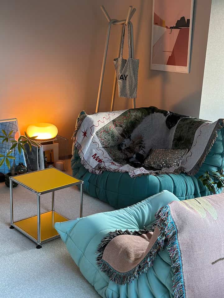 ミント色のソファと黄色いサイドテーブル、温かい間接照明がある居心地の良いリビングルーム