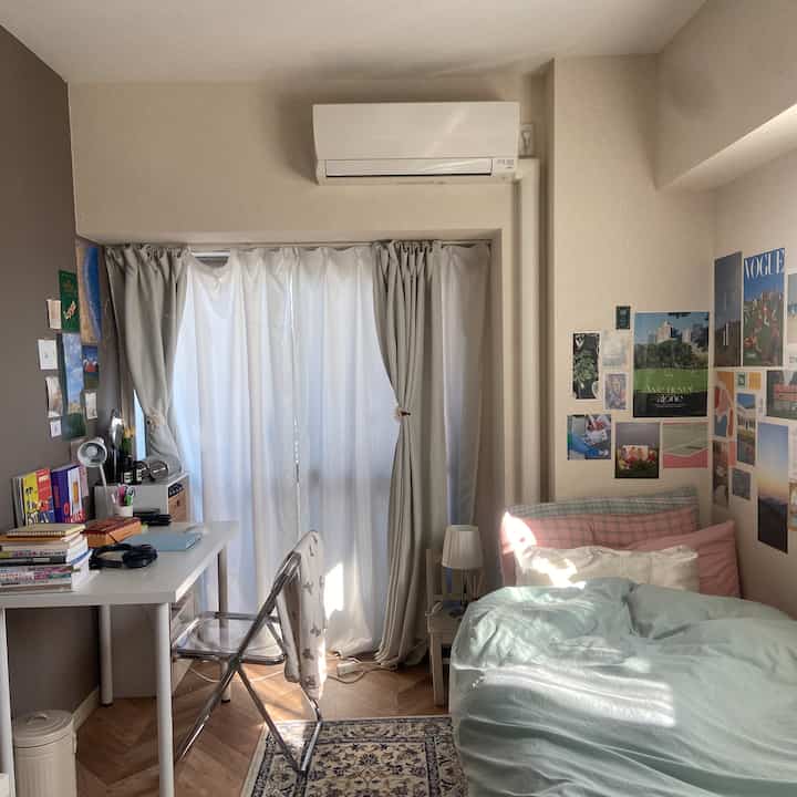 White and gray toned small bedroom featuring desk with folding chair, bed, and wall posters creating a cozy atmosphere