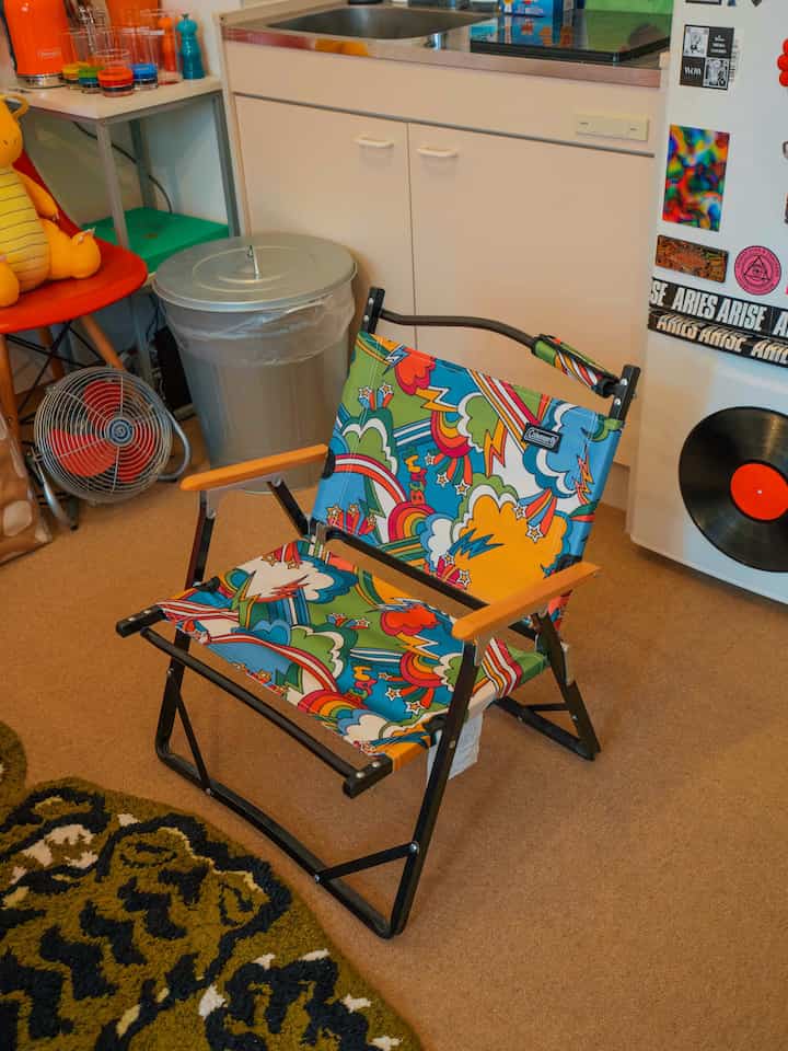 ベージュトーンの床と白いキッチンがある小さなキッチンスペース、カラフルなヴィンテージ柄の椅子とレトロスタイルの小物が配置された雰囲気のあるインテリア