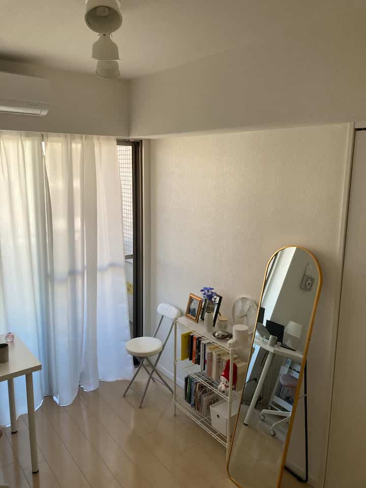 Bright white and gold toned studio apartment with gold-framed full-length mirror and bookshelf in a simple setting