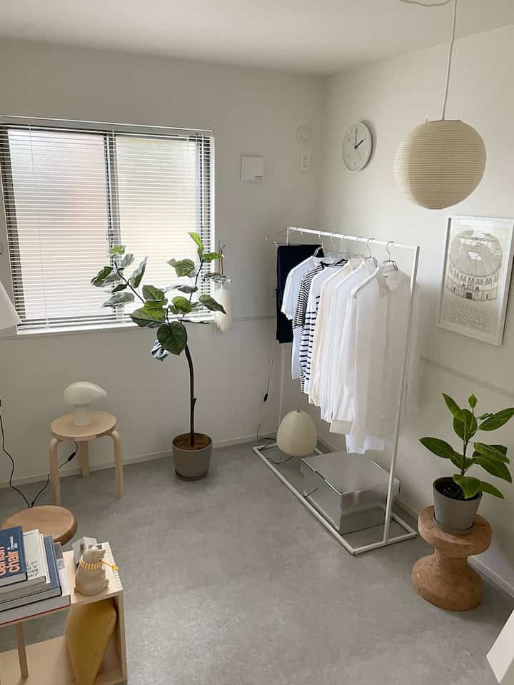 明るい白とナチュラルウッドトーンの小さなリビング、植物と洋服ラックが配置されたシンプルなインテリア