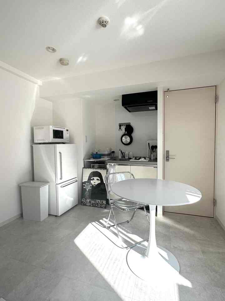Clean white monotone studio kitchen with a round dining table, simple and compact space