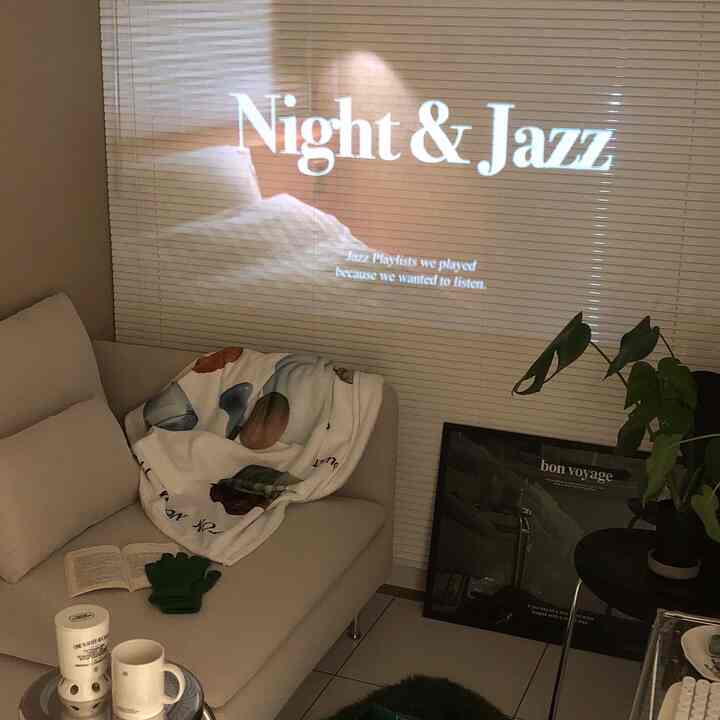 白と茶色のトーンのリビング、ソファの上にブランケットと植物、ブラインドに映し出された映像がある雰囲気のあるインテリア