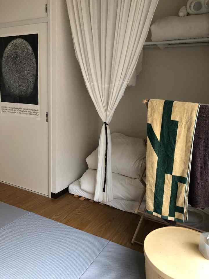 白と木目調のベランダ空間、カーテンで束ねられた寝具とブランケットが置かれた雰囲気のあるインテリア