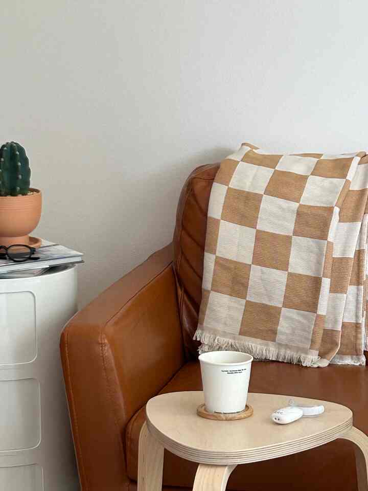ベージュとブラウンの色調のリビング、レザーソファとチェック柄のスローが配置された居心地の良いインテリア