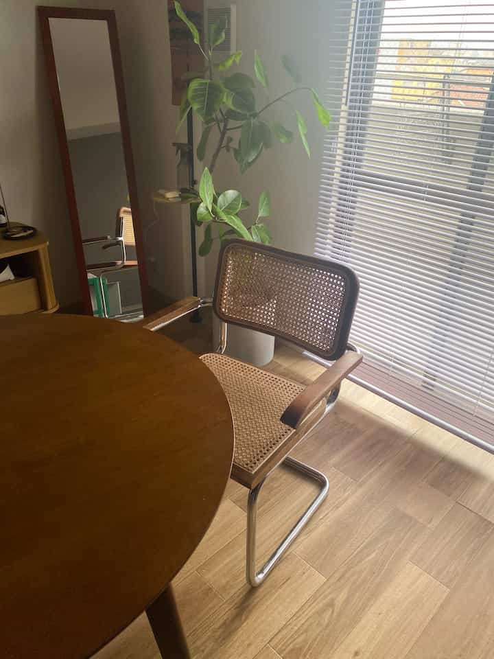 Natural wood-tone dining room by window featuring a round table and a rattan armchair with light-filtering blinds