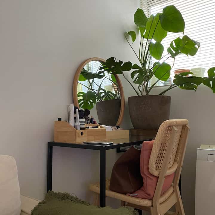 ナチュラルな色調のリビングルームのデスクスペース、ラタンチェアと丸い鏡、緑豊かな植物が温かみのある雰囲気を演出しているインテリア