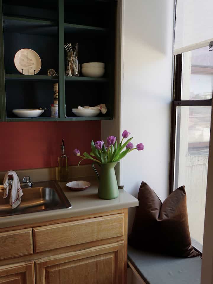 A cozy kitchen featuring white walls and brown wooden cabinets, accented with a green vase holding purple tulips