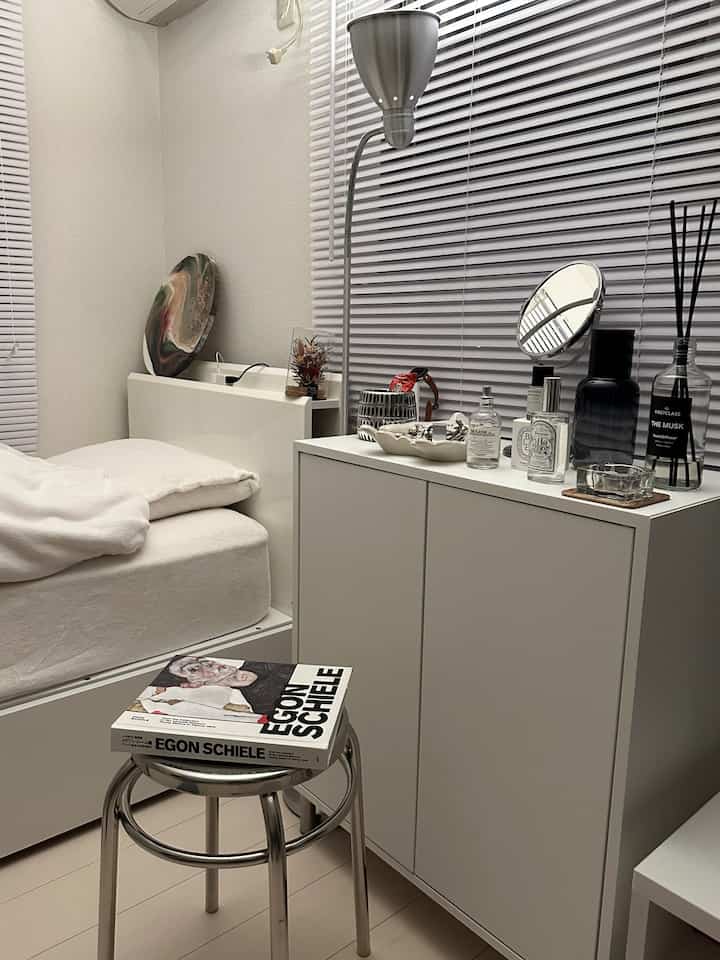 White-toned small bedroom featuring a stainless steel stool and storage cabinet in a simple, minimal interior