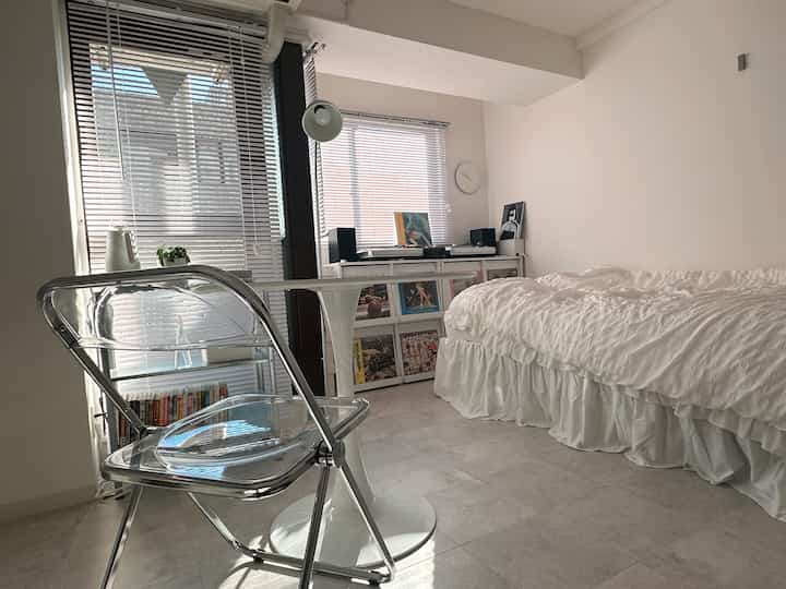 明るい白色調の狭いワンルーム、折り畳みチェアと円形ダイニングテーブル、ベッドが整然と配置されたシンプルなインテリア