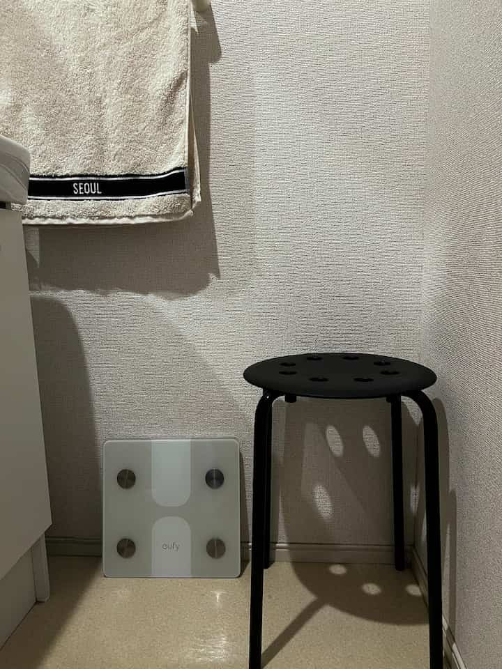 ベージュと白のトーンの浴室、黒いスツールと体重計が置かれた印象的な空間