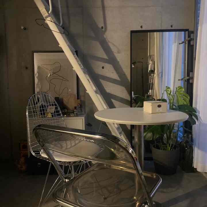 モノトーンのインダストリアルスタイルのコンパクトなワンルーム、丸い白いテーブルとメタリックなダイニングチェア、植物が配置された落ち着いた空間