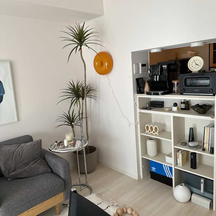 Bright white wall and floor tone living room with gray armchair and large plant beside a small silver side table