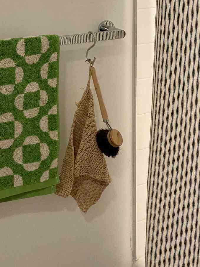 Natural-toned bathroom with green towel and beige brush hanging on a chrome towel rack beside striped wall tiles
