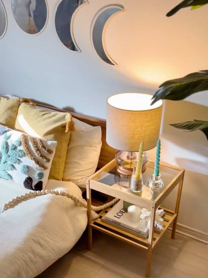 ナチュラルカラーと木目調の寝室、木製のナイトテーブルにテーブルランプとキャンドルが置かれた雰囲気のあるインテリア