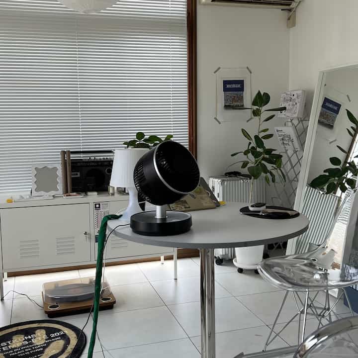 白と黒を基調としたミッドセンチュリーモダンのリビング、シンプルな丸テーブルと透明な椅子、コンパクトなサーキュレーターが置かれた雰囲気ある空間