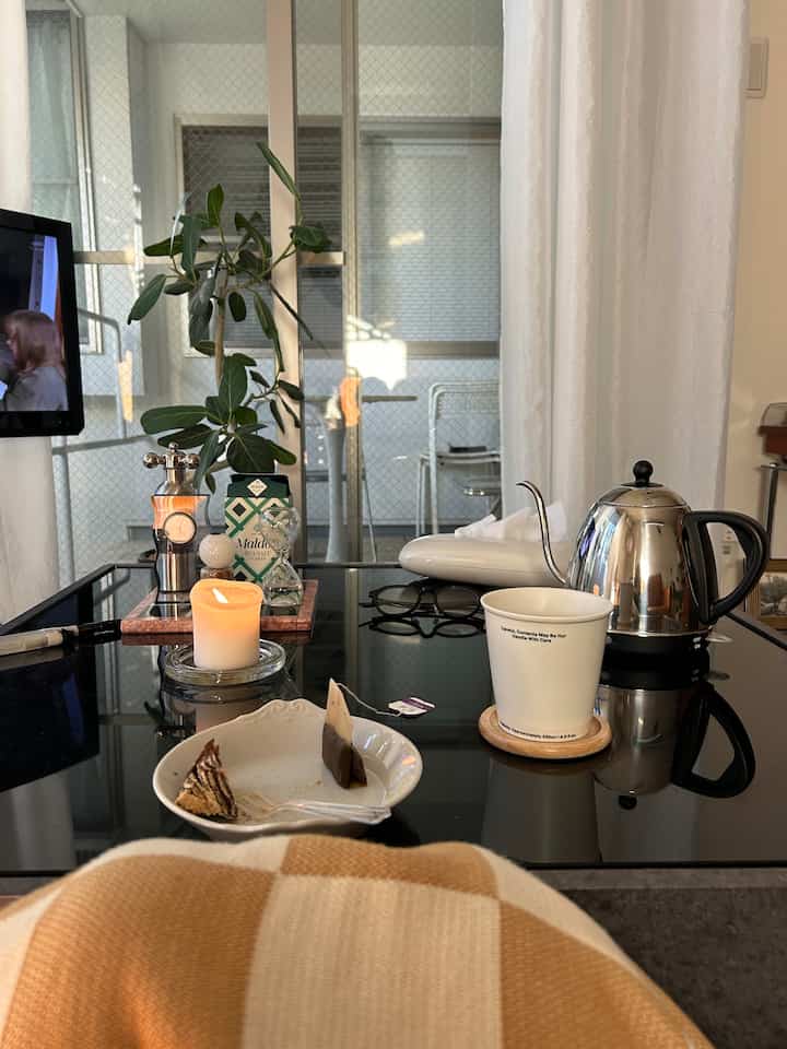 黒いガラステーブルの上にキャンドルとティーカップ、ブラウンチェックのブランケットが置かれた雰囲気のあるおうちカフェ空間