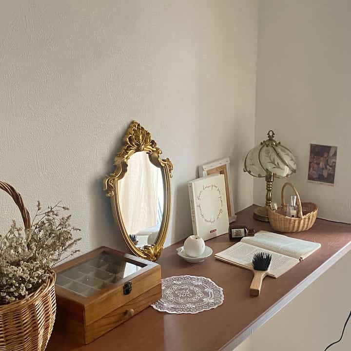 Bright white wall and wood-tone surface featuring a French Country style gold-framed mirror, vintage lamp, and decorative items creating a cozy ambiance